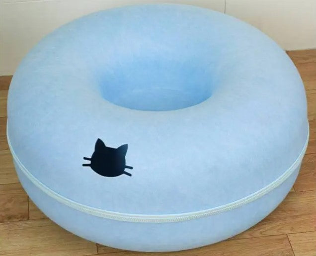 Pale blue round cat tunnel with a recessed center, light trim, and a black cat-head emblem on the front, photographed on a wooden floor.