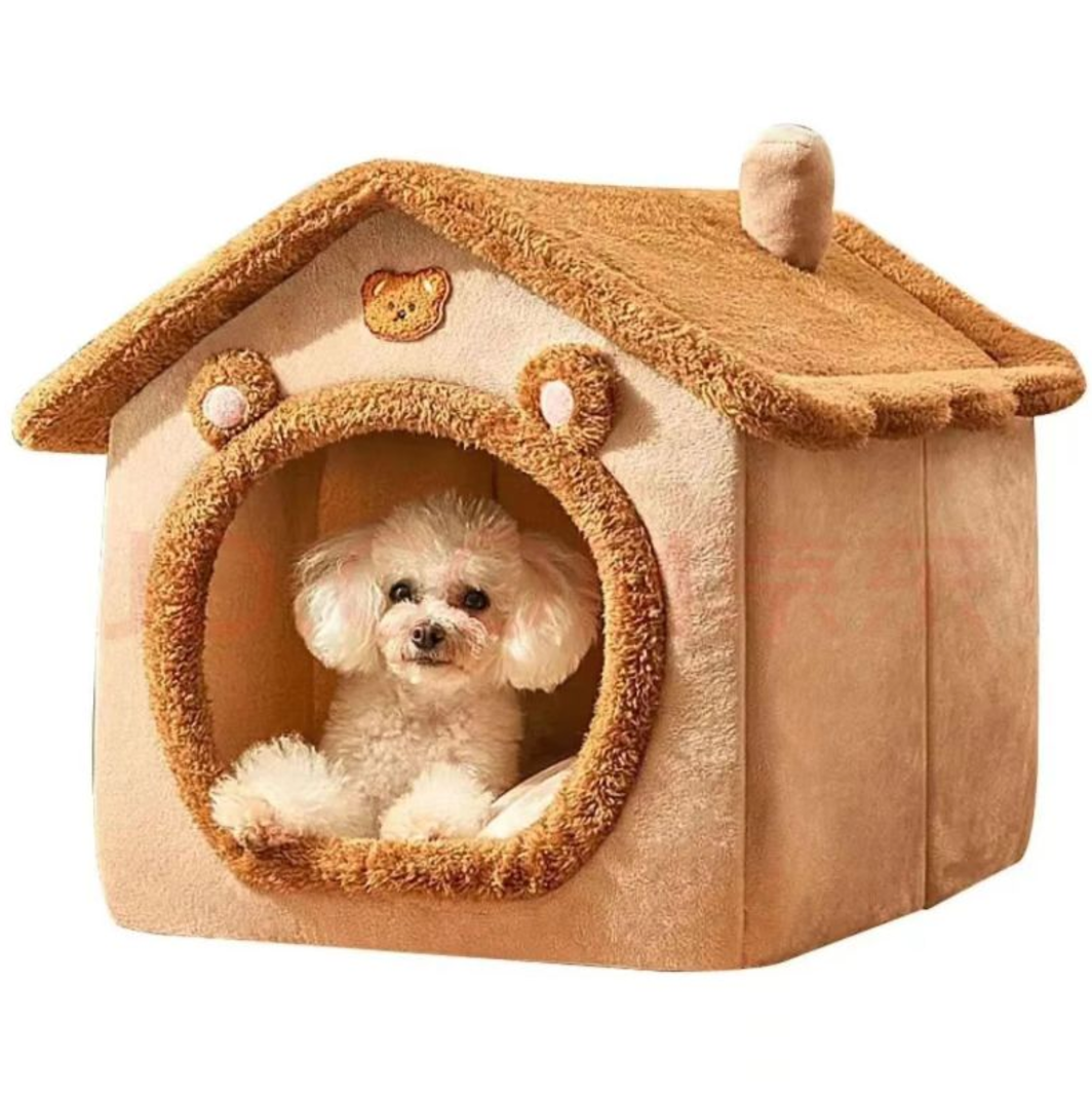 Small white dog sitting inside a tan house-shaped pet bed with a round, trimmed entrance.