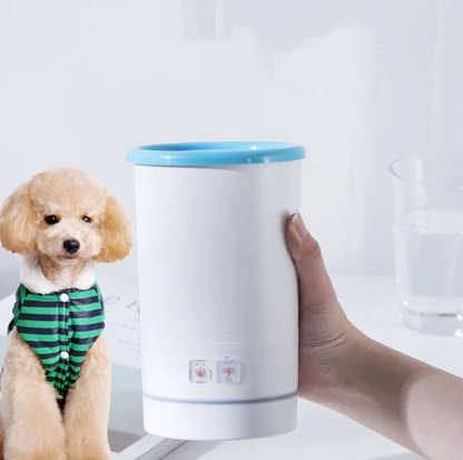 A small light-brown dog in a green striped sweater sits beside a white paw-cleaning cup held upright by a hand.