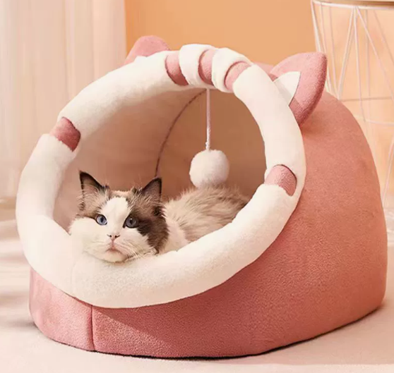 Two cats sitting inside a pink cat bed with a rounded cream-trimmed opening and striped trim.