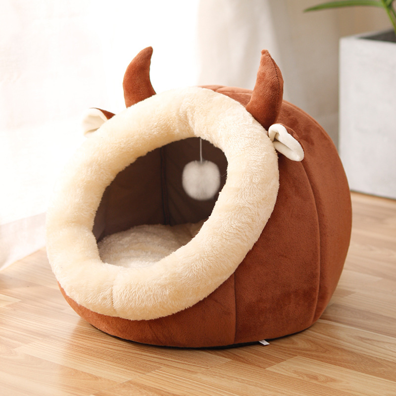 Brown rounded cat bed with a cream oval entrance, pointed ears, and a hanging ball inside.