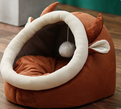 Brown rounded cat bed with a cream oval entrance, brown cushion, and hanging ball.