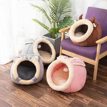 Three rounded cat beds in gray, pink, and brown arranged together on the floor and a chair.