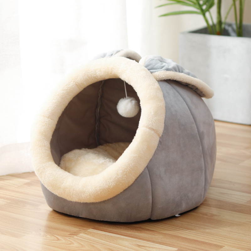 Gray rounded cat bed with a cream oval entrance, fabric ears, and a hanging ball inside.