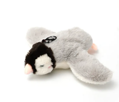 Grey plush animal lying on its side, with a black-and-white face, pink details and a black loop on its back.